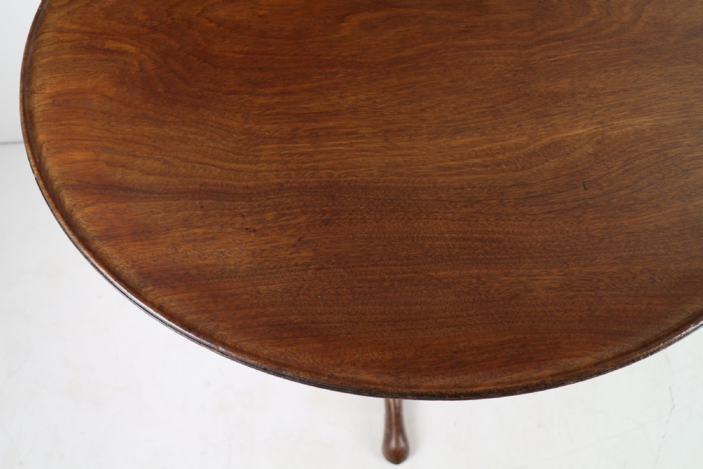 An Early Georgian mahogany tripod table featuring a circular dish top tilted vertically above a turned stem and cabriole legs with pad feet. View XIV