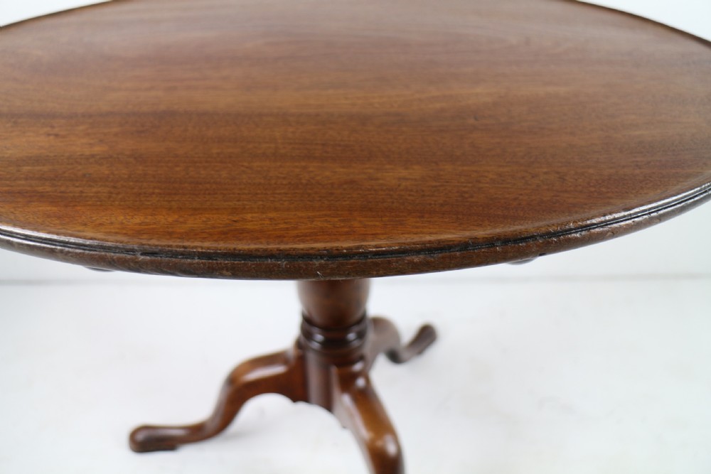 An Early Georgian mahogany tripod table featuring a circular dish top tilted vertically above a turned stem and cabriole legs with pad feet. View XVII