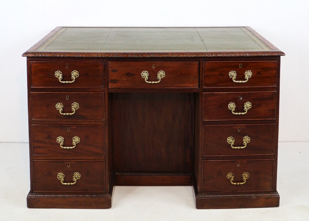 A dark mahogany kneehole library desk featuring multiple drawers with brass drop handles and panelled sides. View III