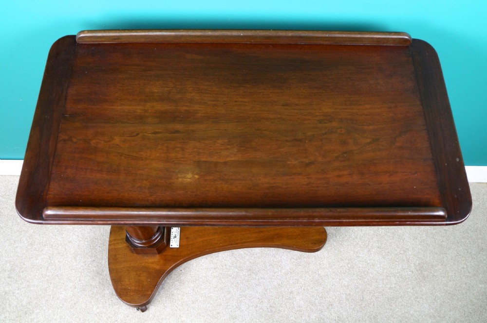 A Victorian mahogany adjustable reading table featuring a ratchet height mechanism, tilted top ledge, turned pedestal, and curved base on castors. View X