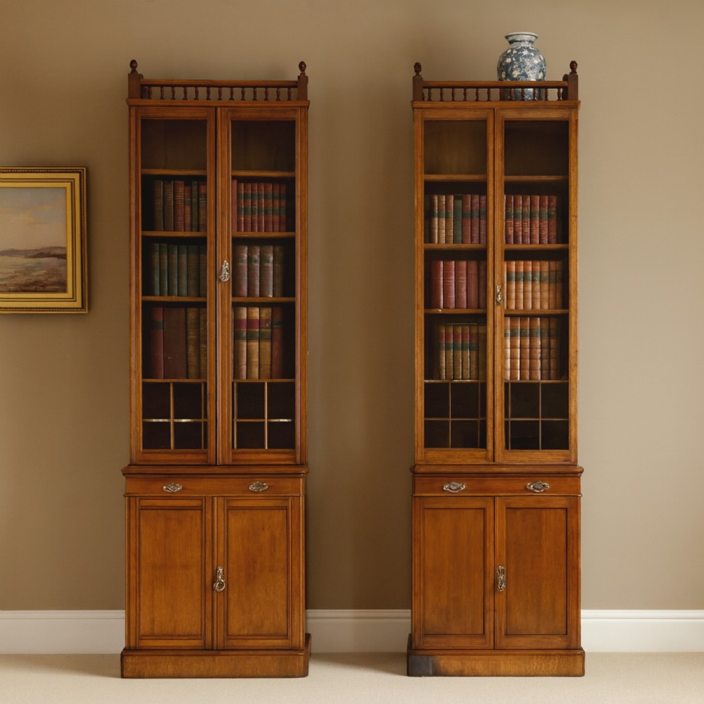 A pair of tall, narrow late Victorian oak glazed bookcases with spindle gallery tops and lower panelled cupboard bases.