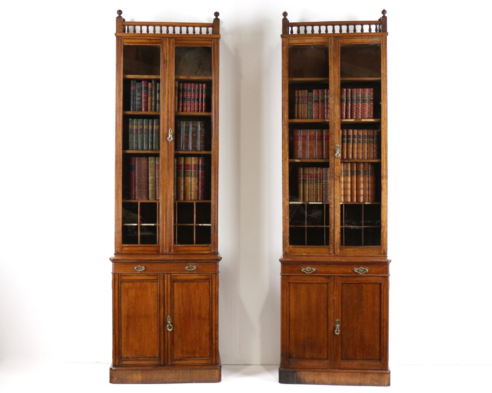 A pair of tall, narrow late Victorian oak glazed bookcases with spindle gallery tops and lower panelled cupboard bases. View II
