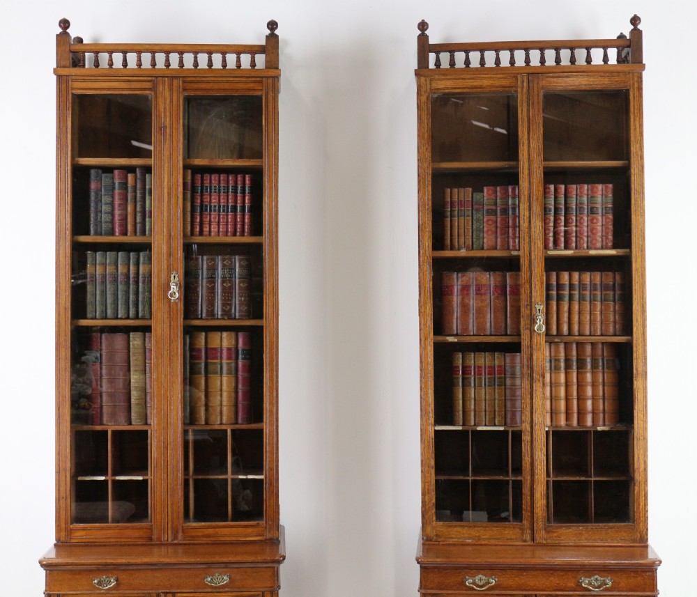 A pair of tall, narrow late Victorian oak glazed bookcases with spindle gallery tops and lower panelled cupboard bases. View V