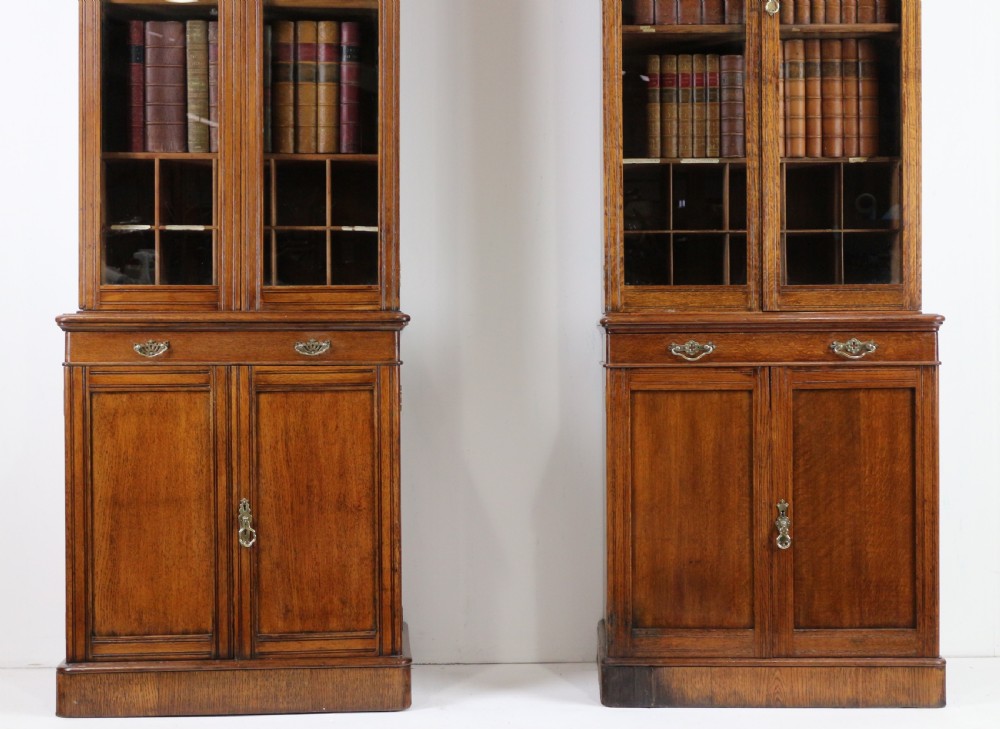 A pair of tall, narrow late Victorian oak glazed bookcases with spindle gallery tops and lower panelled cupboard bases. View VI
