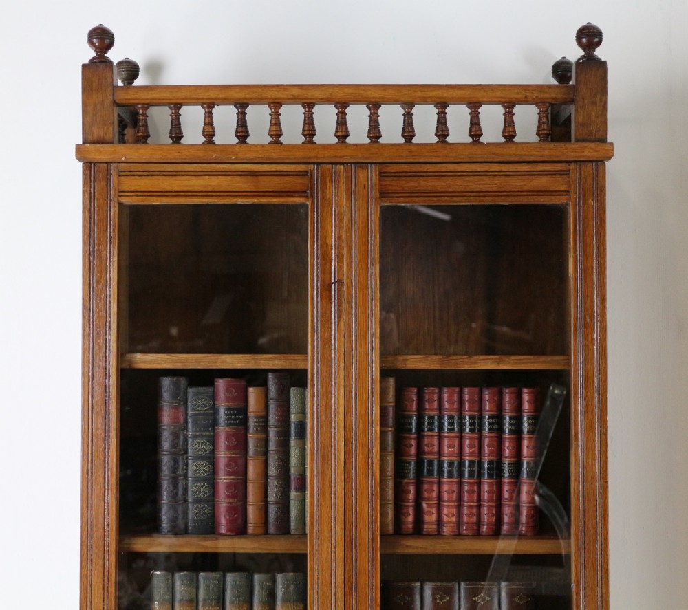 A pair of tall, narrow late Victorian oak glazed bookcases with spindle gallery tops and lower panelled cupboard bases. View XIII
