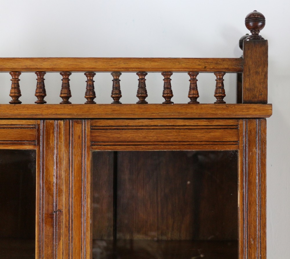 A pair of tall, narrow late Victorian oak glazed bookcases with spindle gallery tops and lower panelled cupboard bases. View XV