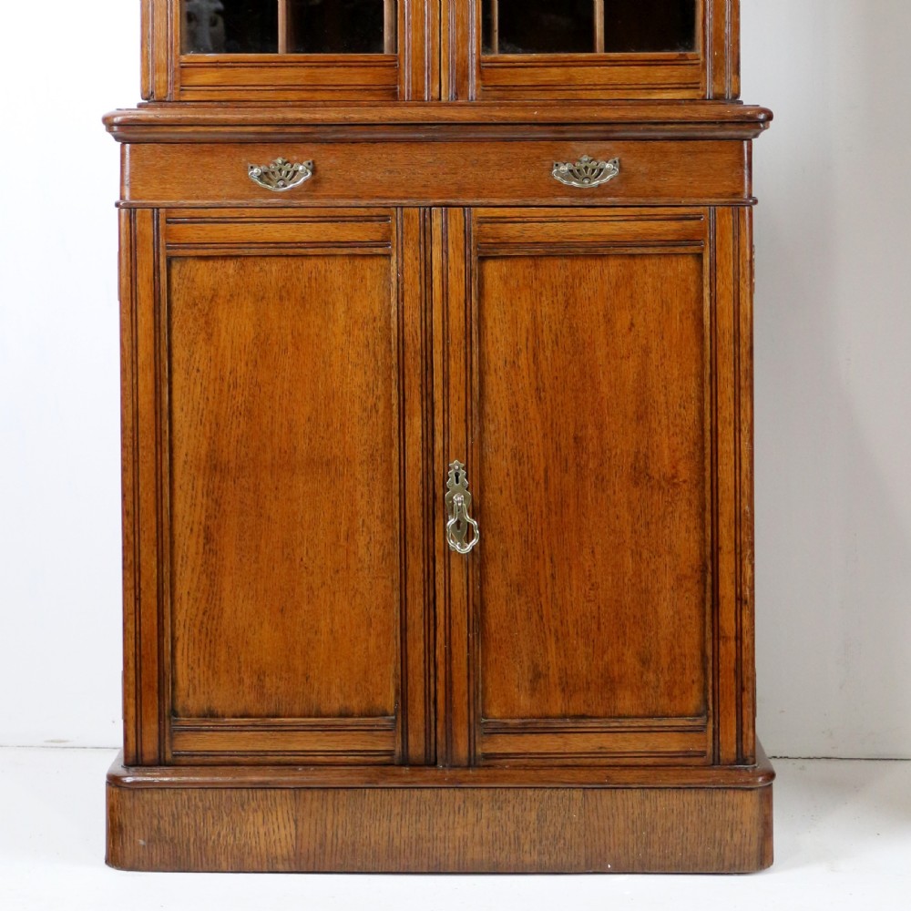 A pair of tall, narrow late Victorian oak glazed bookcases with spindle gallery tops and lower panelled cupboard bases. View XVIII