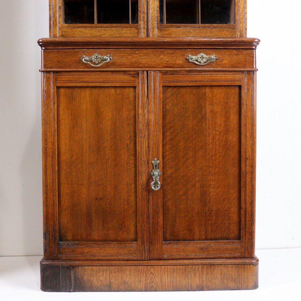 A pair of tall, narrow late Victorian oak glazed bookcases with spindle gallery tops and lower panelled cupboard bases. View XIX