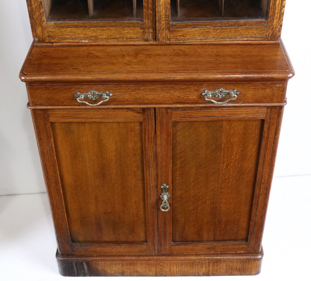 A pair of tall, narrow late Victorian oak glazed bookcases with spindle gallery tops and lower panelled cupboard bases. View XXI
