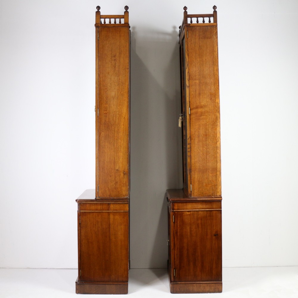 A pair of tall, narrow late Victorian oak glazed bookcases with spindle gallery tops and lower panelled cupboard bases. View XXIX