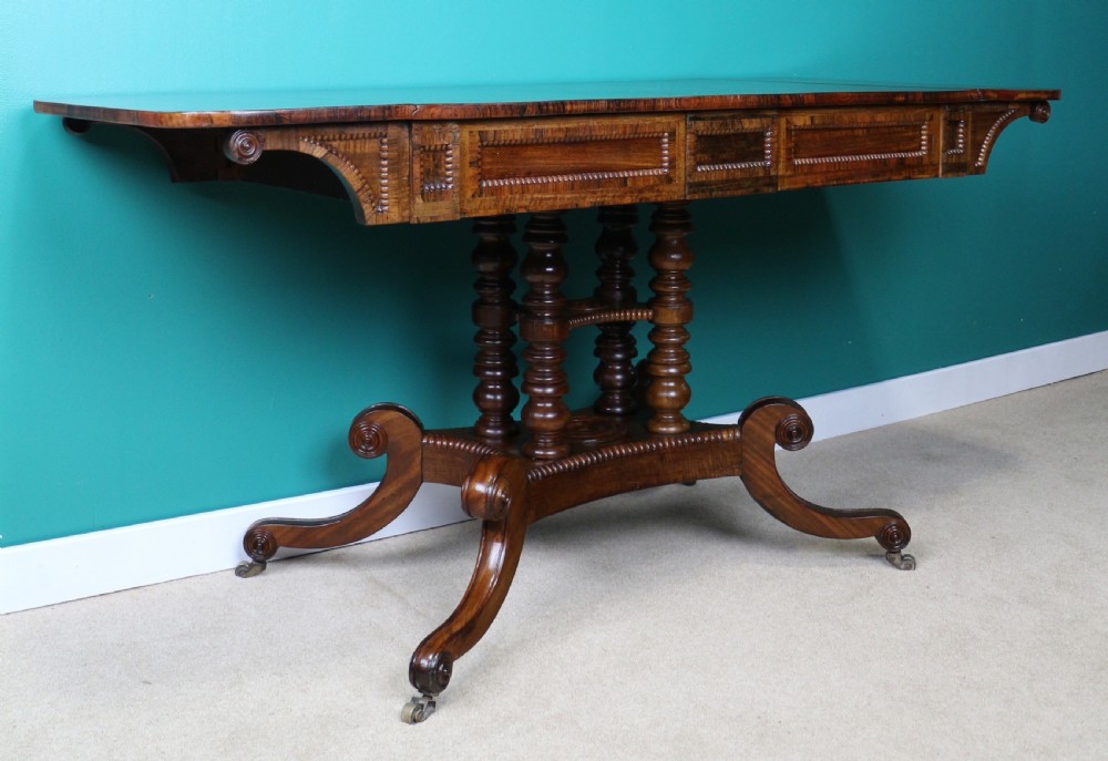 A Regency mahogany and rosewood crossbanded sofa table featuring drop leaves, bead-moulded frieze drawers, turned support pillars, and splayed legs on brass castors. View III