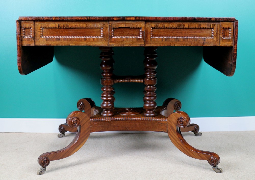 A Regency mahogany and rosewood crossbanded sofa table featuring drop leaves, bead-moulded frieze drawers, turned support pillars, and splayed legs on brass castors. View XVIII