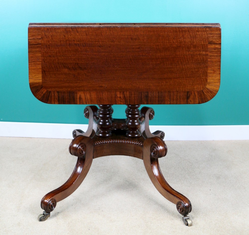 A Regency mahogany and rosewood crossbanded sofa table featuring drop leaves, bead-moulded frieze drawers, turned support pillars, and splayed legs on brass castors. View XXIX