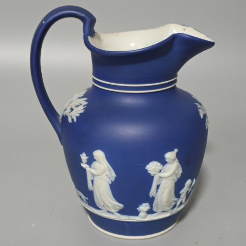 fig 2. A cobalt blue stoneware jug featuring white raised neoclassical figures in relief with a high arched handle and curved spout.