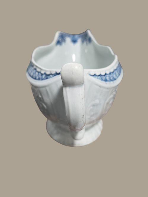 fig 1. An eighteenth-century blue and white soft-paste porcelain sauce boat featuring moulded scroll decoration, a shaped rim, a scroll handle, and a printed landscape scene.