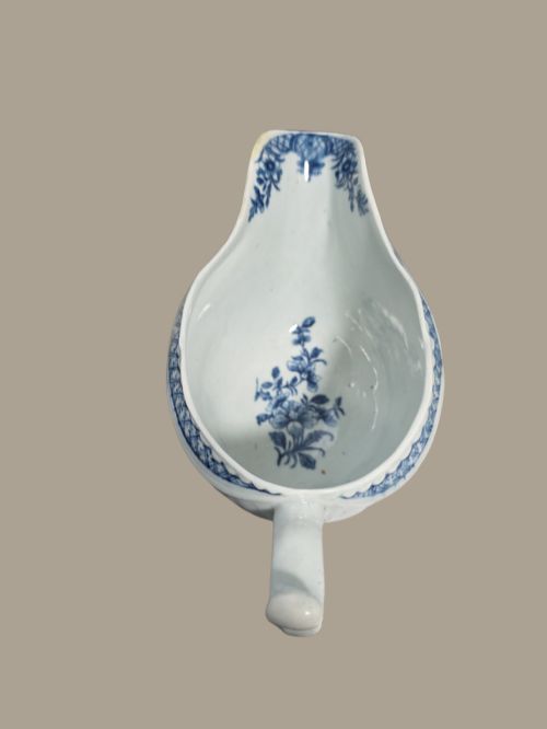 fig 3. An eighteenth-century blue and white soft-paste porcelain sauce boat featuring moulded scroll decoration, a shaped rim, a scroll handle, and a printed landscape scene.