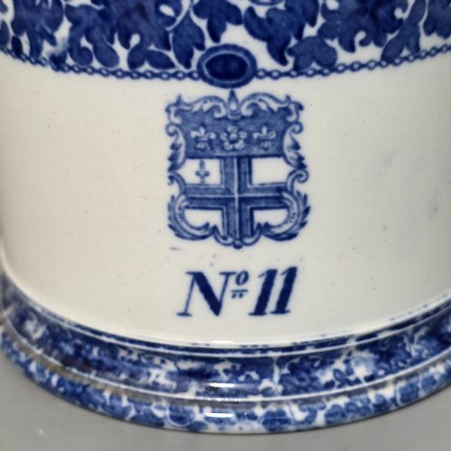 fig 2. A cylindrical blue and white transferware ceramic tankard featuring a floral upper border and a coat of arms crest with the text No 11.