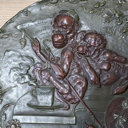 fig 3. An oval dark brown Austrian terracotta relief plaque depicting a satirical scene of an anthropomorphic monkey family framed by relief floral motifs.