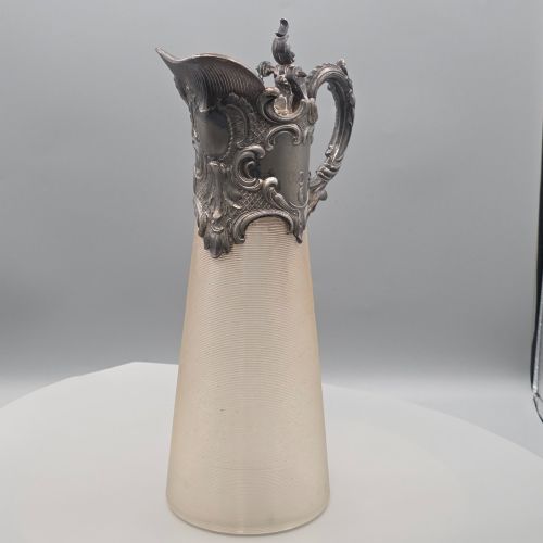 fig 2. An antique French Rococo style silver-plated claret jug featuring a tapered ribbed clear glass body and an ornate scrolling silver spout and handle.