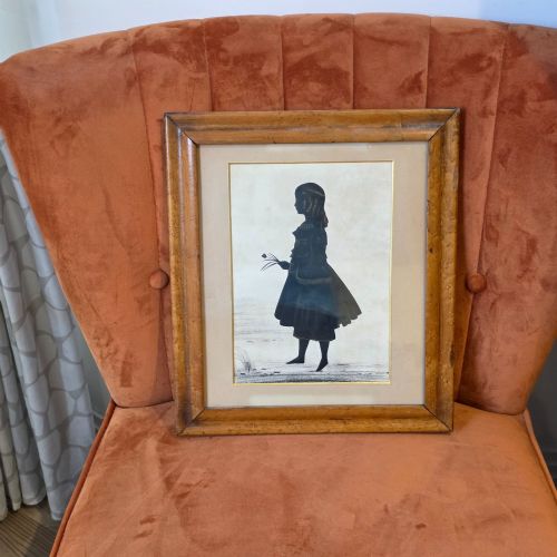 fig 1. A 19th-century full-length cut-paper silhouette portrait of a young girl holding flowers, displayed in a glazed wooden frame with a gold inner slip.