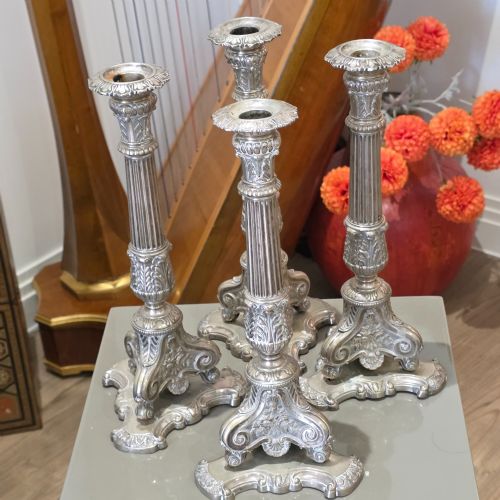 fig 1. A set of four silver candlesticks with fluted columns and ornate leaf details set on molded tripod bases.