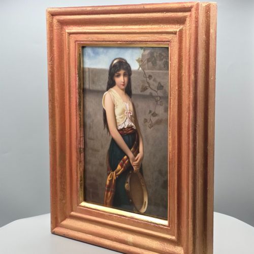 fig 2. A rectangular hand-painted porcelain plaque depicting a young woman with a tambourine, set within a thick moulded gilt frame.