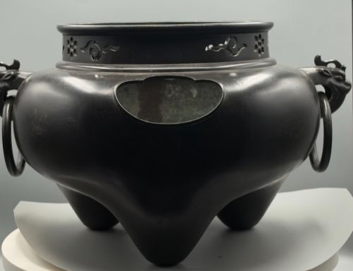 fig 1. A dark patinated bronze tripod tea brazier featuring cast lion mask handles with loose ring pulls and pierced decorative motifs along the collar.