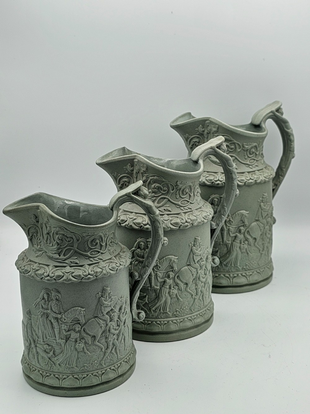 A set of three graduated sage green ceramic jugs decorated with detailed relief-moulded scenes of knights and foliate scrollwork. View II