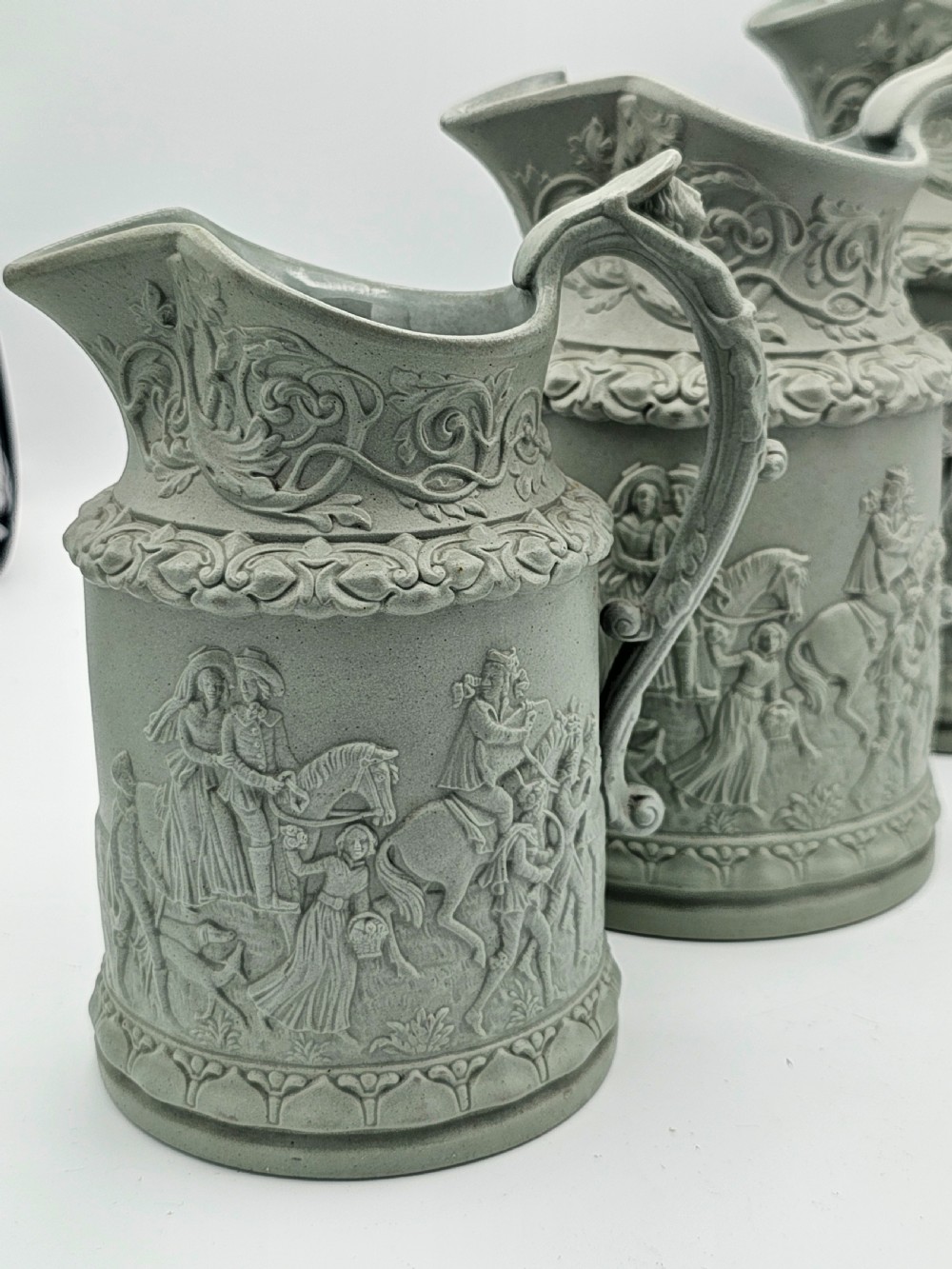 A set of three graduated sage green ceramic jugs decorated with detailed relief-moulded scenes of knights and foliate scrollwork. View III
