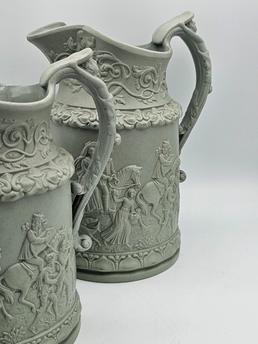 A set of three graduated sage green ceramic jugs decorated with detailed relief-moulded scenes of knights and foliate scrollwork. View VI