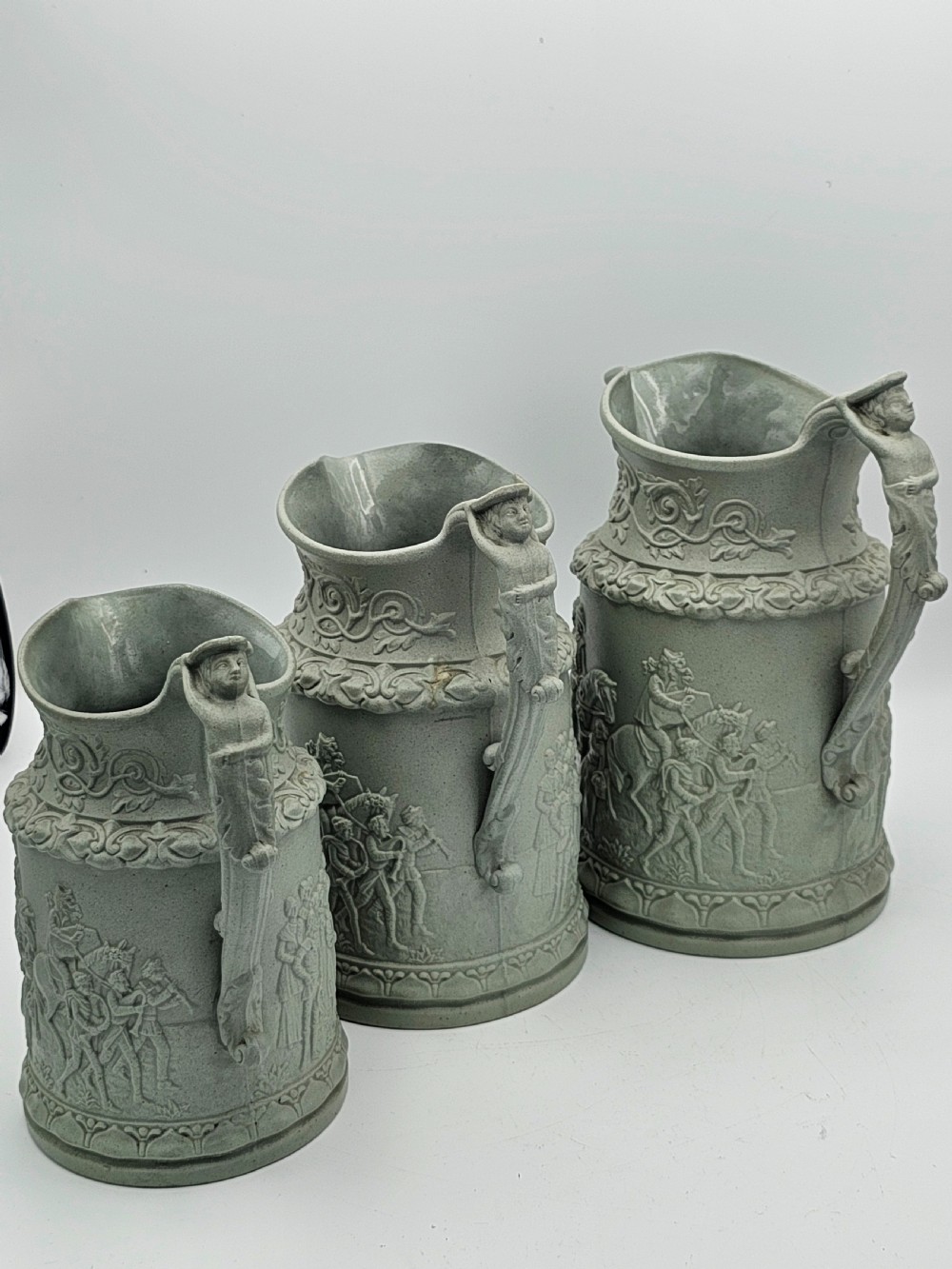 A set of three graduated sage green ceramic jugs decorated with detailed relief-moulded scenes of knights and foliate scrollwork. View VII