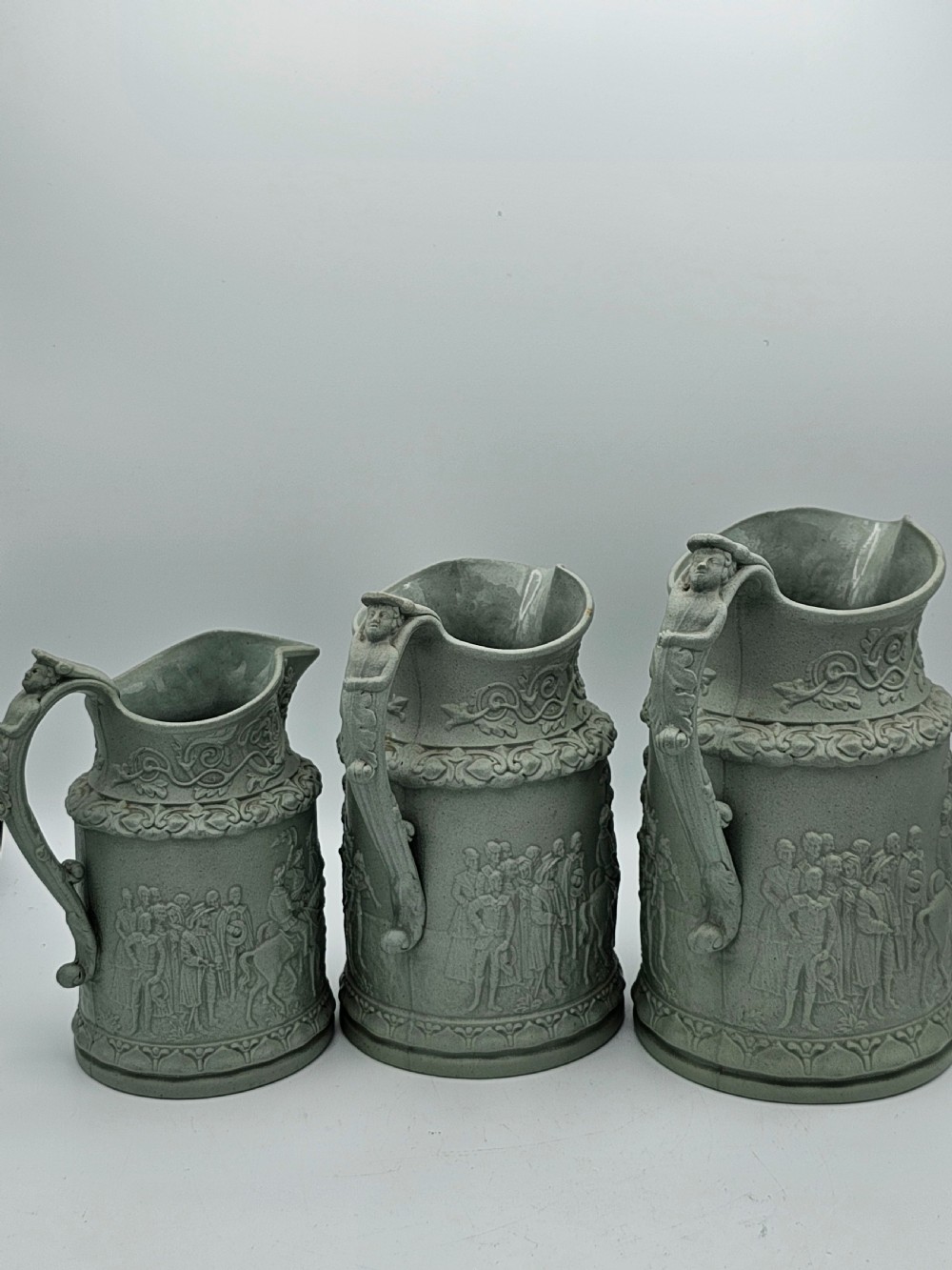 A set of three graduated sage green ceramic jugs decorated with detailed relief-moulded scenes of knights and foliate scrollwork. View VIII
