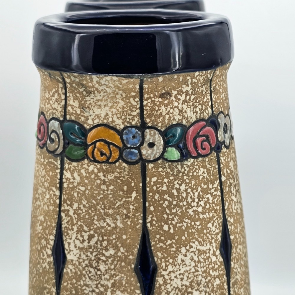 A pair of cylindrical Austrian ceramic vases featuring a textured beige ground, black rim, vertical cutouts, and colourful enamelled floral bands. View V