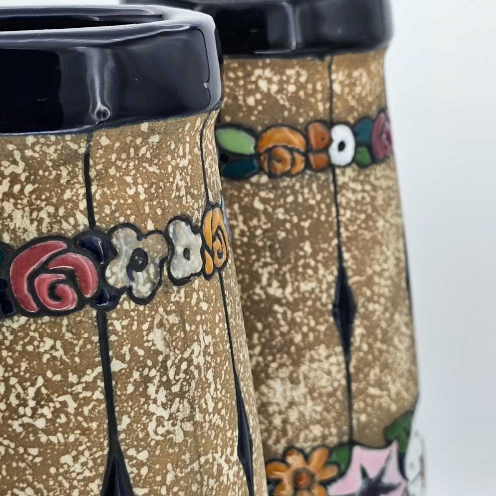 A pair of cylindrical Austrian ceramic vases featuring a textured beige ground, black rim, vertical cutouts, and colourful enamelled floral bands. View VI