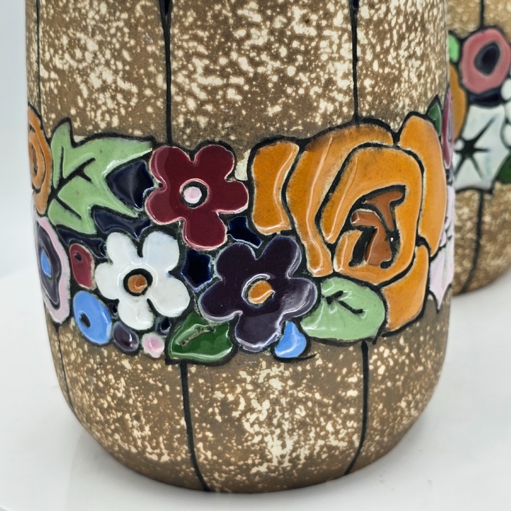A pair of cylindrical Austrian ceramic vases featuring a textured beige ground, black rim, vertical cutouts, and colourful enamelled floral bands. View IX
