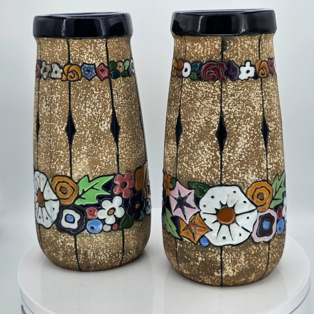 A pair of cylindrical Austrian ceramic vases featuring a textured beige ground, black rim, vertical cutouts, and colourful enamelled floral bands.