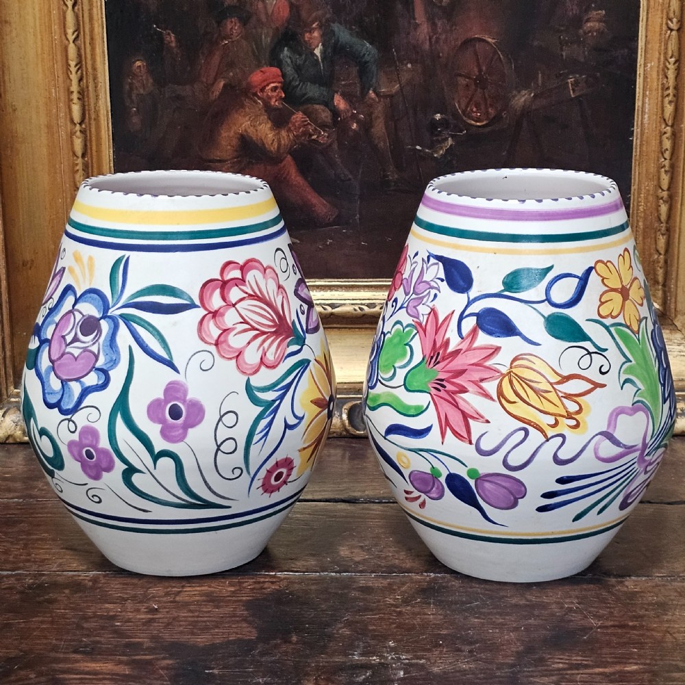 A pair of ovoid off-white ceramic vases decorated with hand-painted floral motifs in pink, purple, blue, green, and yellow.