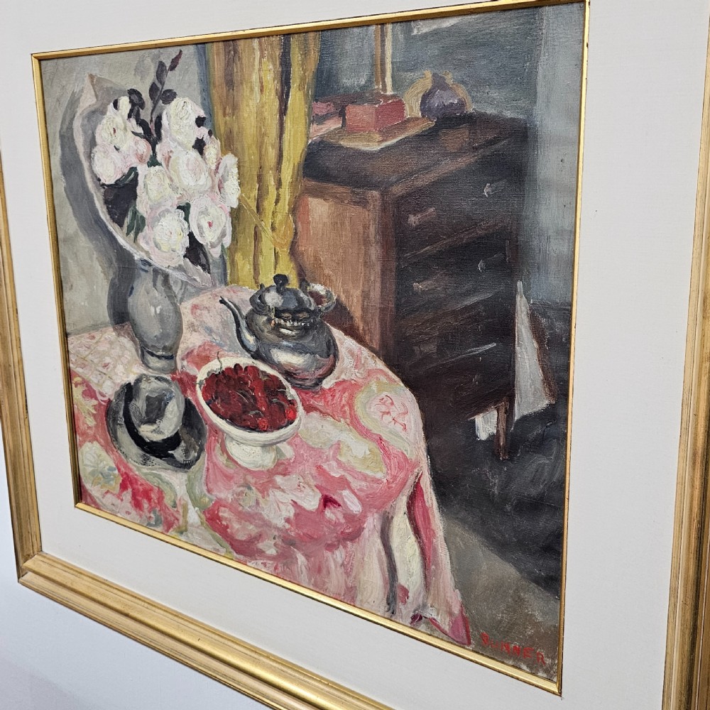 A framed oil painting depicting a detailed still life scene with a vase of white flowers, a teapot, a bowl of cherries, and a hat on a pink patterned tablecloth. View V