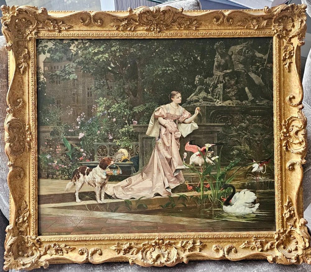 An 1880 framed oil painting depicting a woman in a pink dress beside a garden fountain with birds, presented in a heavily carved gilded frame.