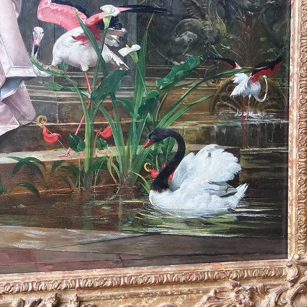 An 1880 framed oil painting depicting a woman in a pink dress beside a garden fountain with birds, presented in a heavily carved gilded frame. View IV