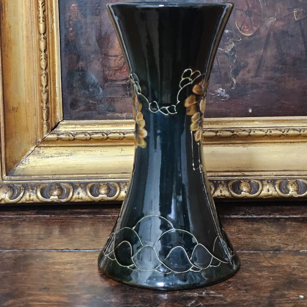 A dark green glazed earthenware vase with a flared top and base, featuring tube-lined ochre floral motifs and geometric line patterns. View III