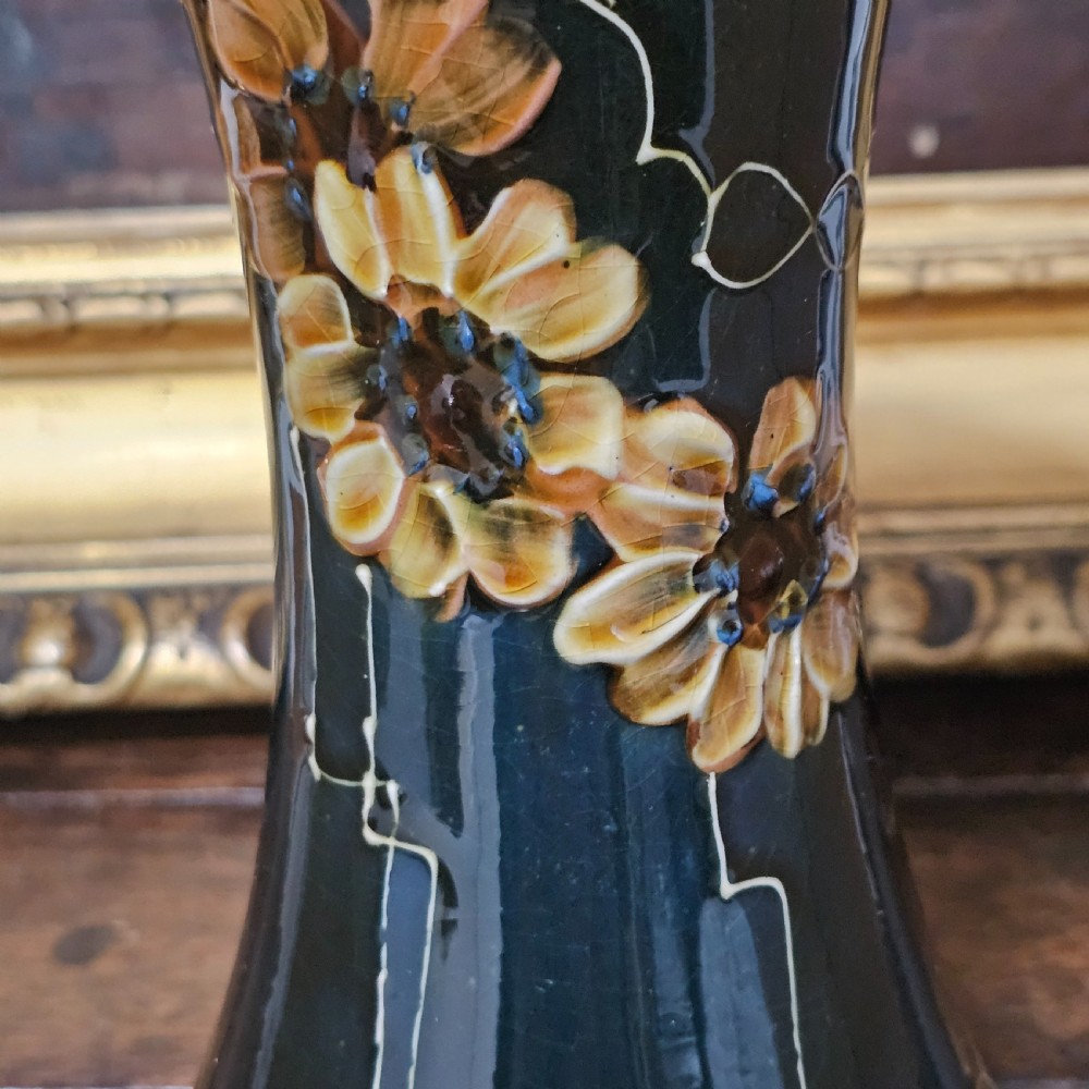 A dark green glazed earthenware vase with a flared top and base, featuring tube-lined ochre floral motifs and geometric line patterns. View V