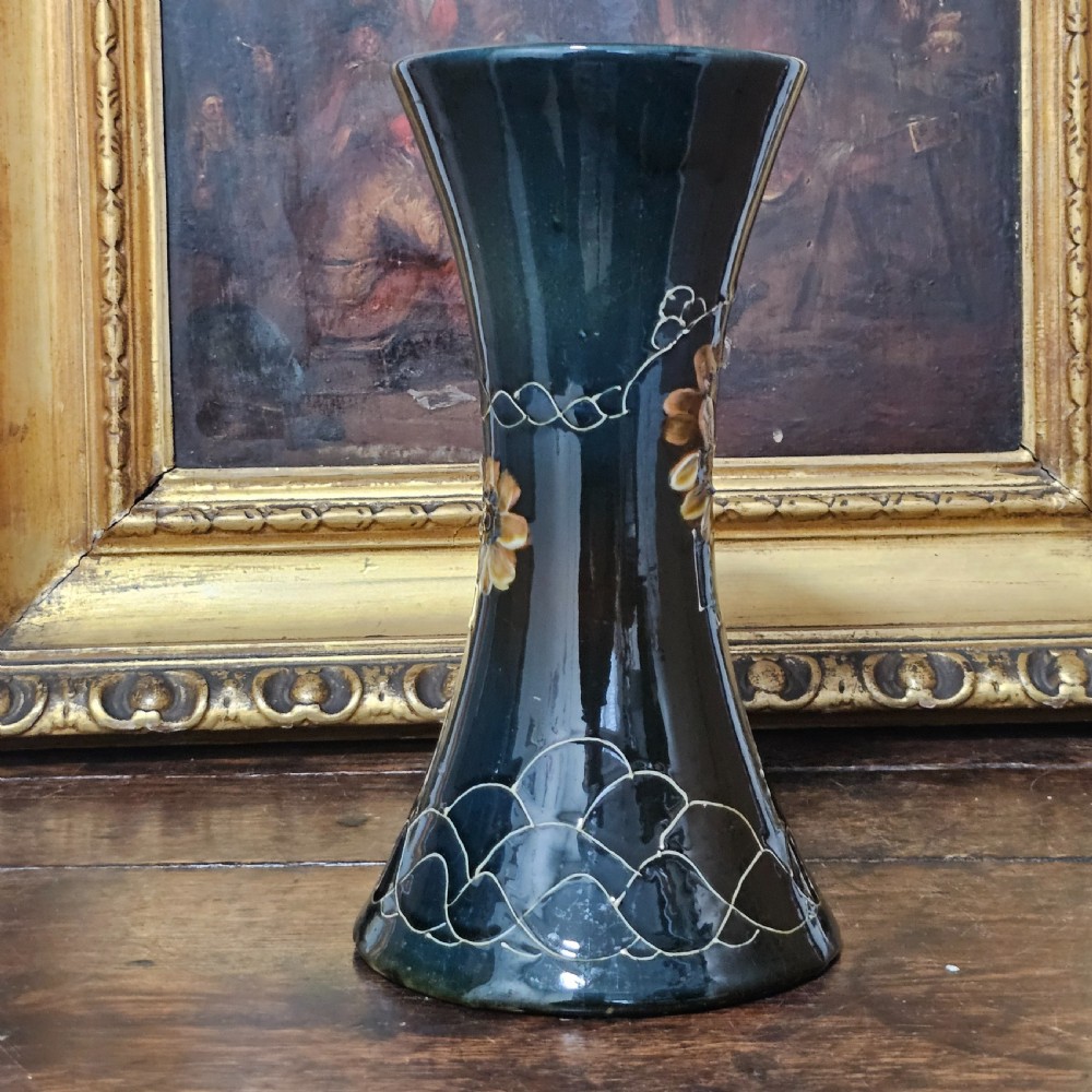 A dark green glazed earthenware vase with a flared top and base, featuring tube-lined ochre floral motifs and geometric line patterns. View VI