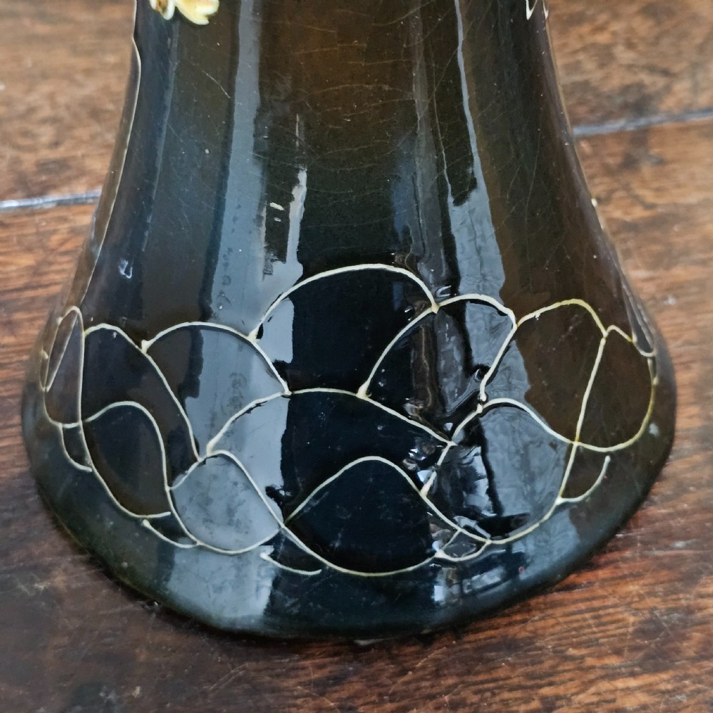 A dark green glazed earthenware vase with a flared top and base, featuring tube-lined ochre floral motifs and geometric line patterns. View VII
