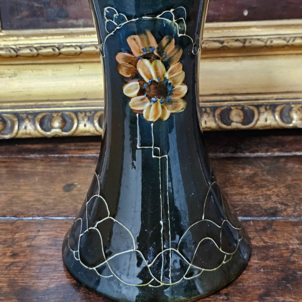 A dark green glazed earthenware vase with a flared top and base, featuring tube-lined ochre floral motifs and geometric line patterns. View IX
