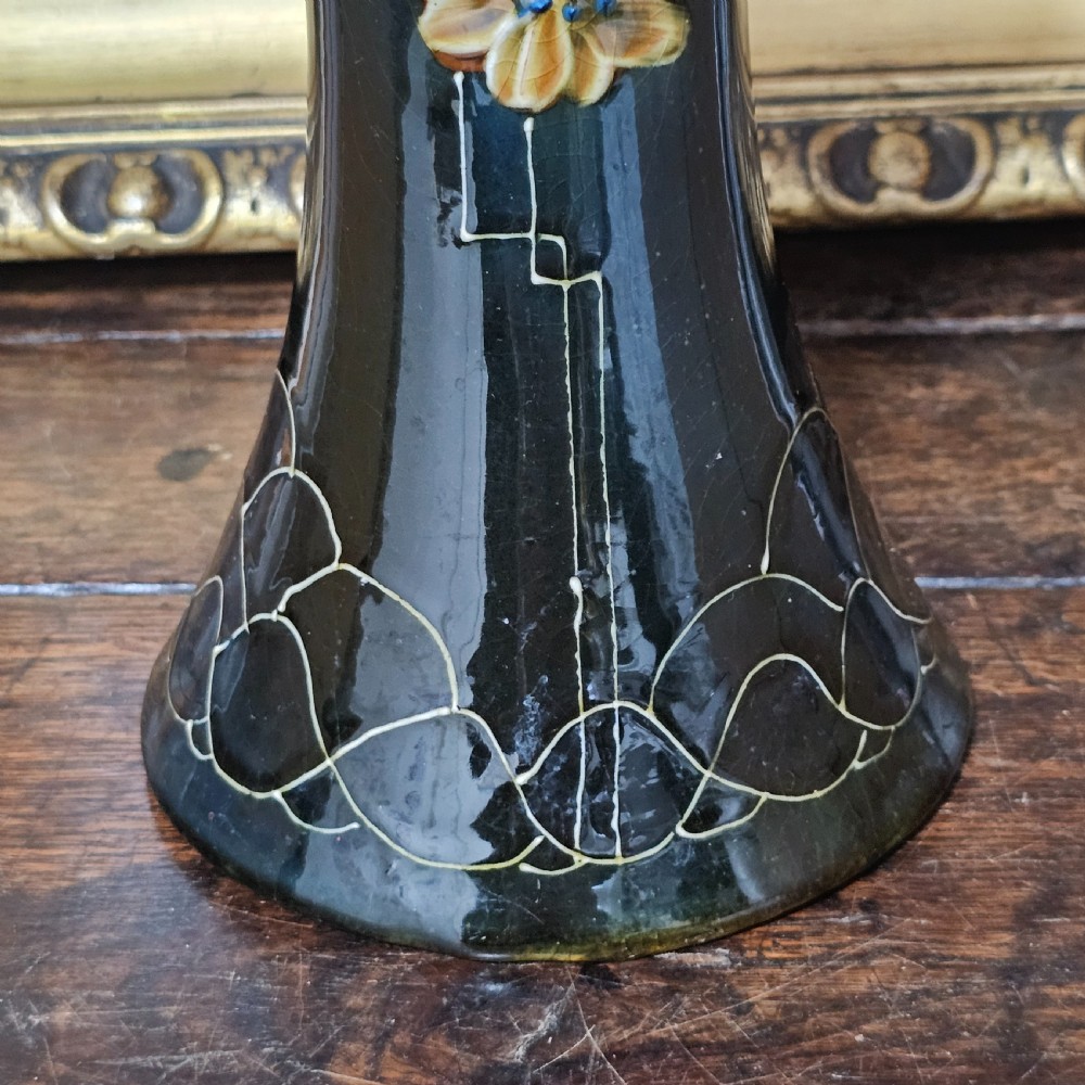 A dark green glazed earthenware vase with a flared top and base, featuring tube-lined ochre floral motifs and geometric line patterns. View X