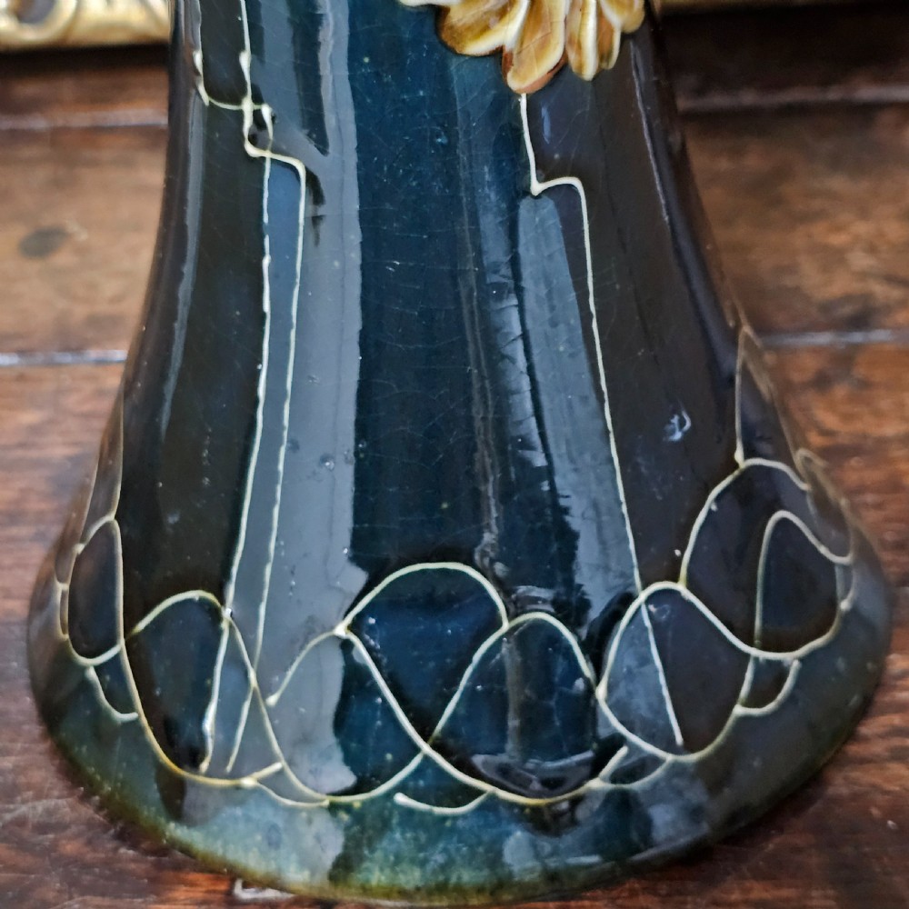 A dark green glazed earthenware vase with a flared top and base, featuring tube-lined ochre floral motifs and geometric line patterns. View XII