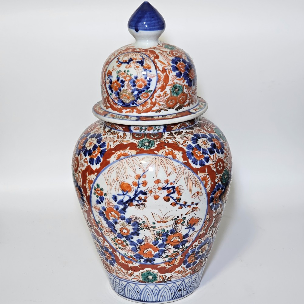 A 19th-century Japanese Imari porcelain ginger jar with a domed finial lid, decorated in hand-painted iron-red and cobalt blue floral cartouches.