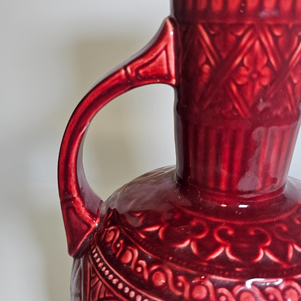 A dark red glazed earthenware jug featuring relief-moulded geometric patterns, a bulbous lower section, a fluted neck, and a curved handle. View III