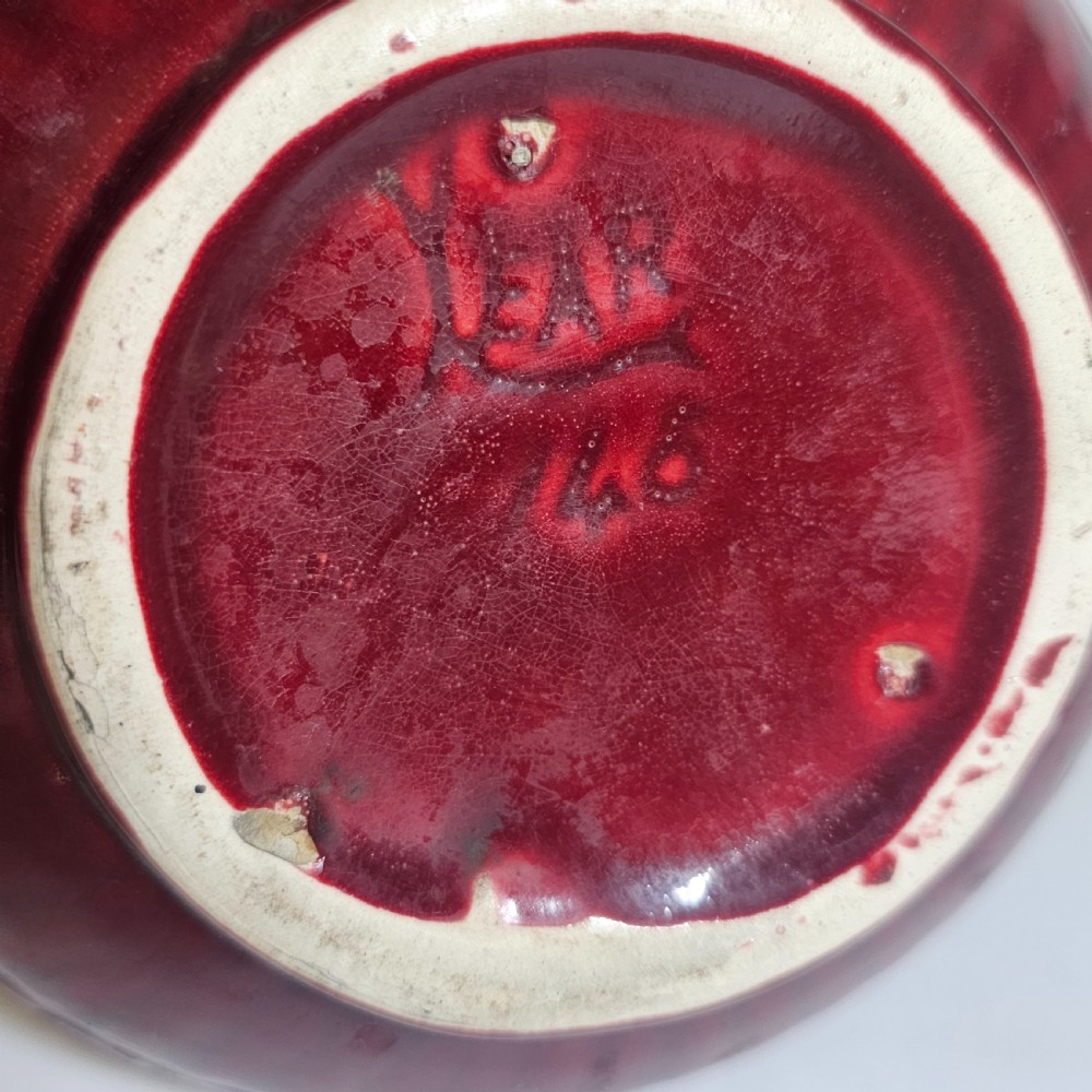 A dark red glazed earthenware jug featuring relief-moulded geometric patterns, a bulbous lower section, a fluted neck, and a curved handle. View V